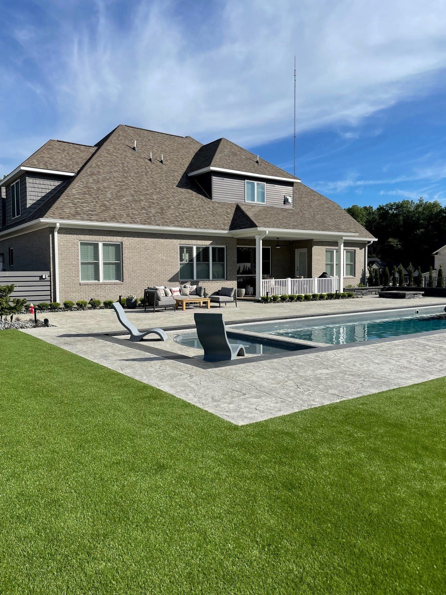 Custom fiberglass pool with stone patio and mature landscape surround
